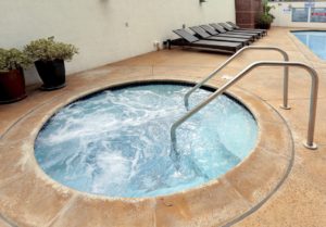 Jacuzzi in swimming pool enclosure near lounge chairs.