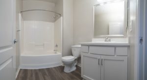 Apartment bathroom with wood plank flooring, shower tub combo with curved shower rod, toilet, and cabinet storage space under the sink